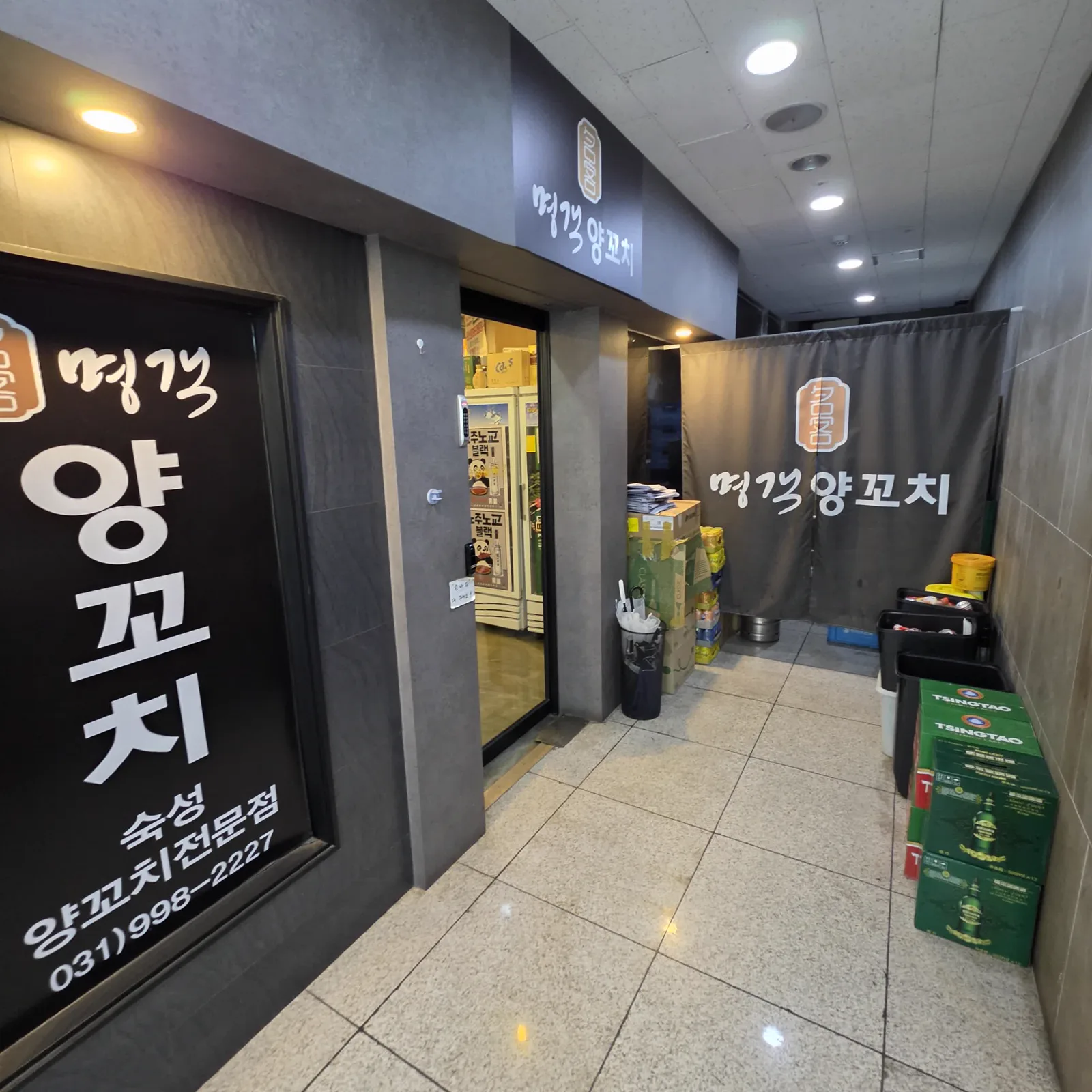 숙성 양꼬치 전문점 명객양꼬치 입구 간판과 옆 복도의 주류 박스