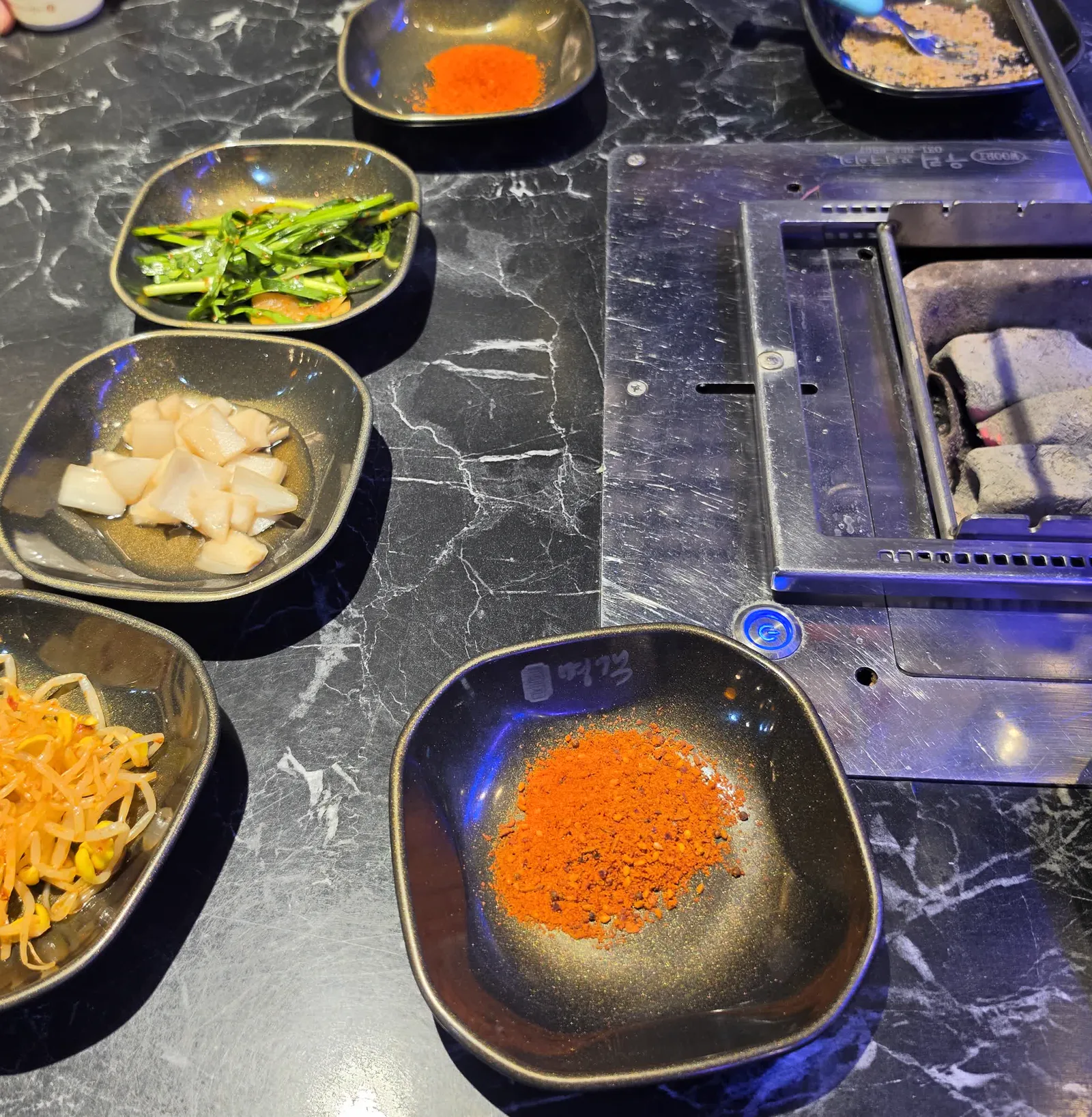 검은 대리석 테이블 위 부추무침 콩나물 하얀 절임 쯔란 가루와 숯 화로