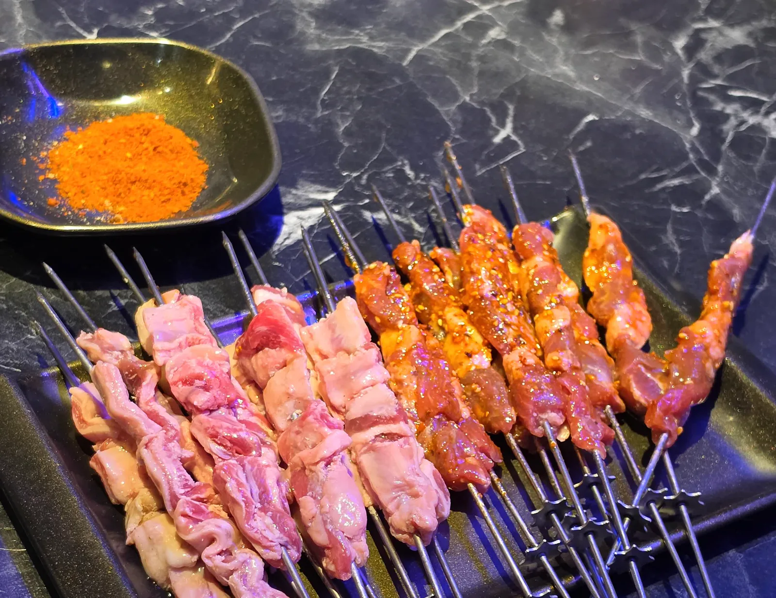 양념이 옅은 양갈비살 꼬치와 붉은 양념 양꼬치가 나란히 담긴 검은 접시