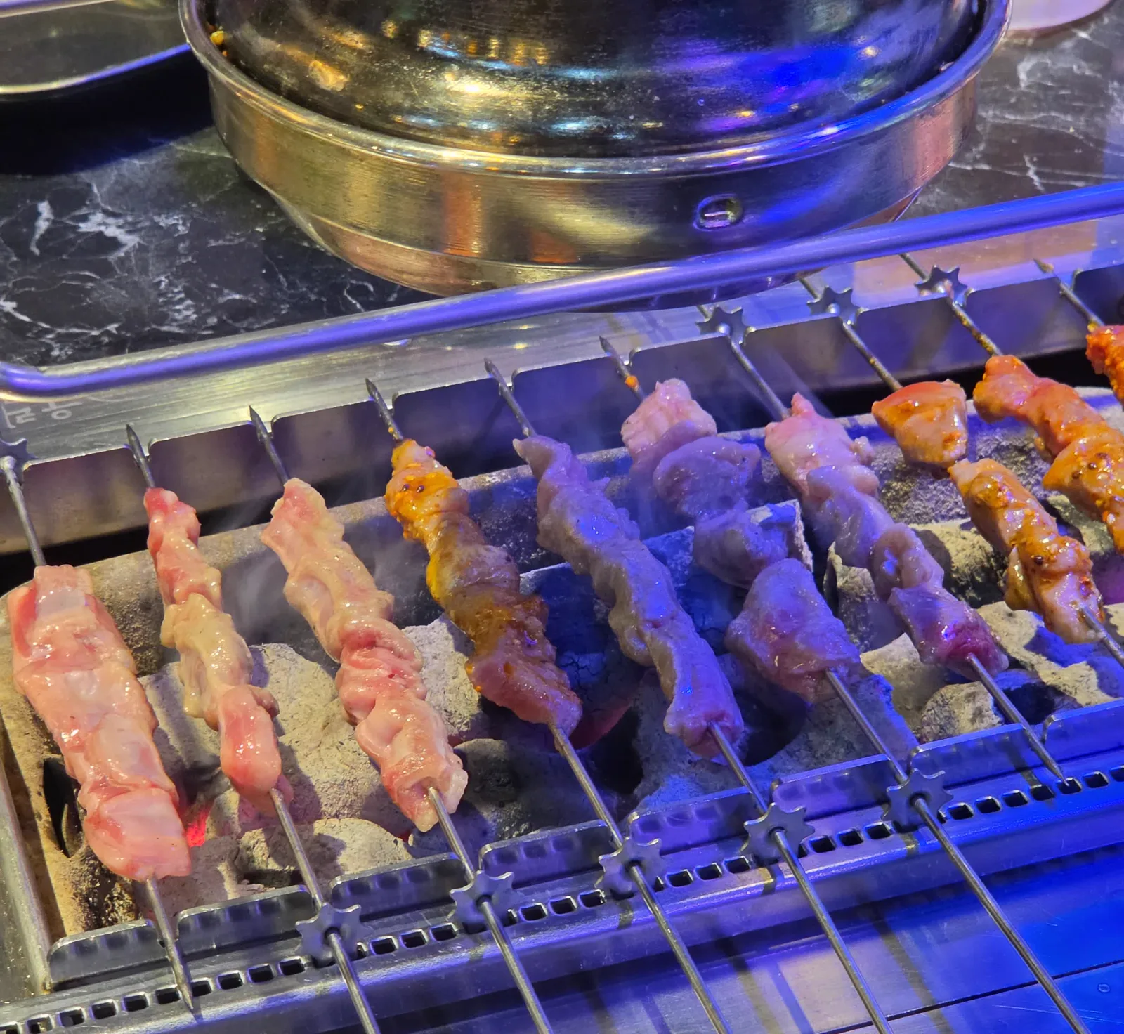 참숯 화로 위 쇠꼬치에서 별 모양 톱니가 맞물린 채 구워지는 양꼬치